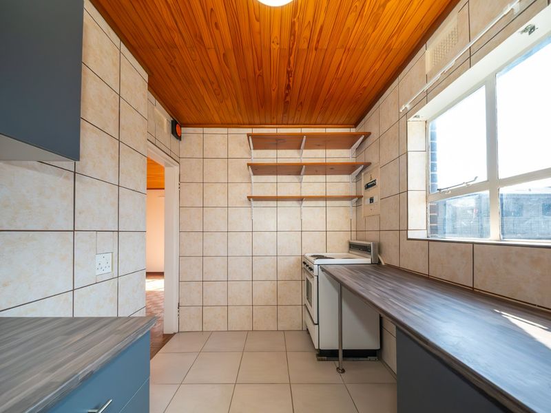 A functional kitchen featuring tiled walls, laminate countertops, a built-in stove, and a distinctive wooden ceiling, offering a clean and practical workspace.