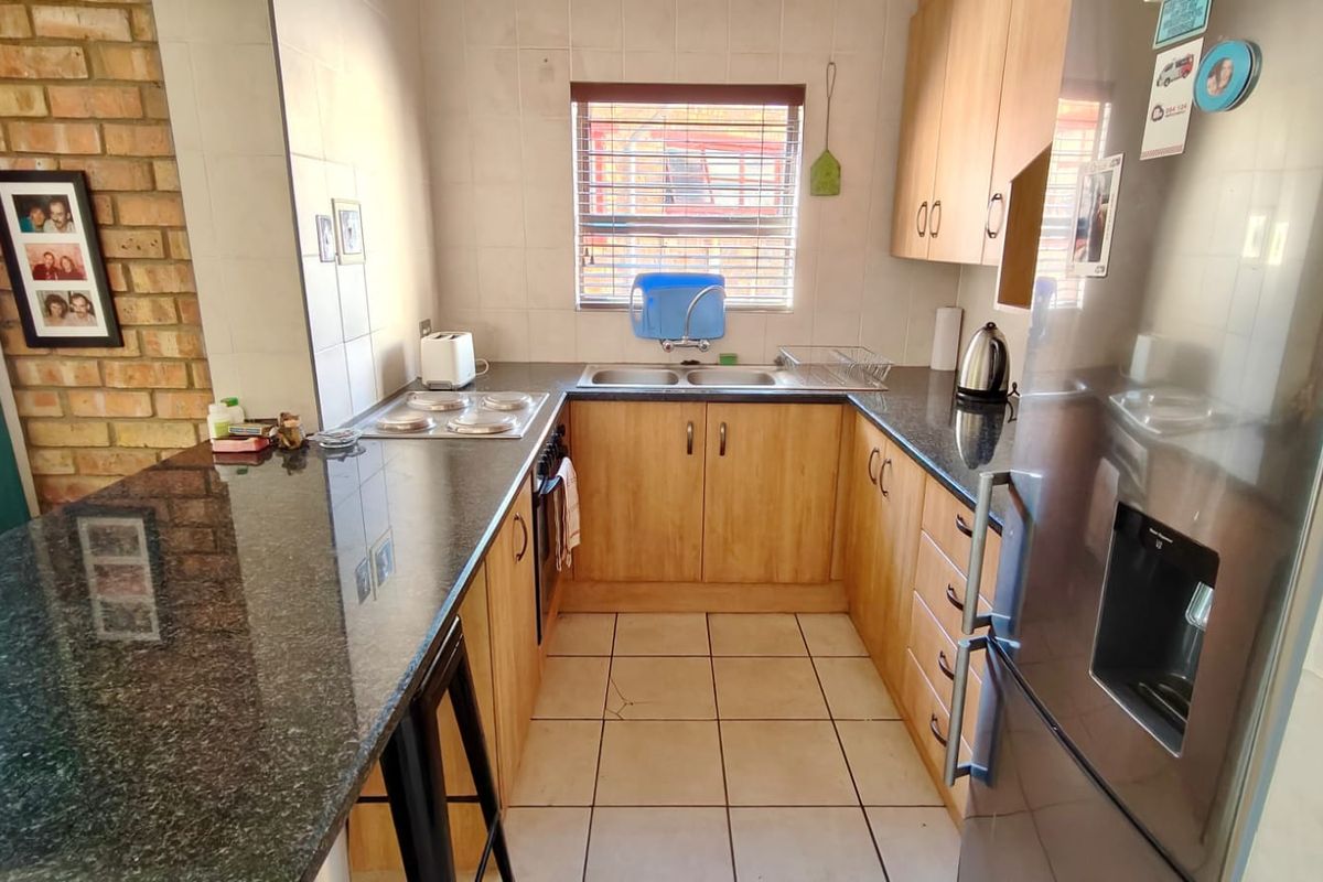 Functional kitchen featuring granite countertops, light wood cabinetry, an electric hob, and a distinctive exposed brick feature wall.