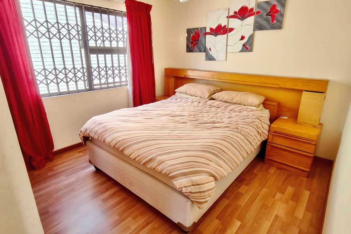 A bedroom featuring laminate flooring, a built-in wooden headboard, and a window fitted with a security gate.