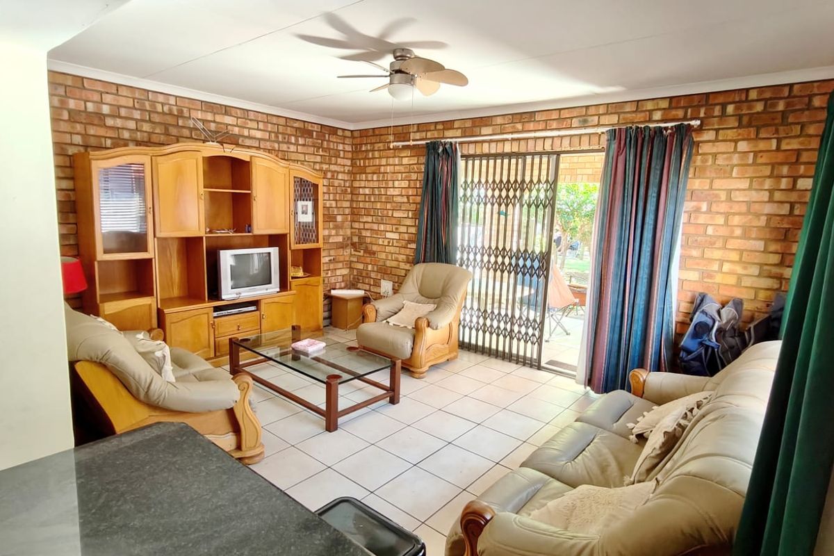 A living room featuring exposed brick walls, tiled flooring, and a ceiling fan, with direct access to the outdoor area through a sliding glass door.