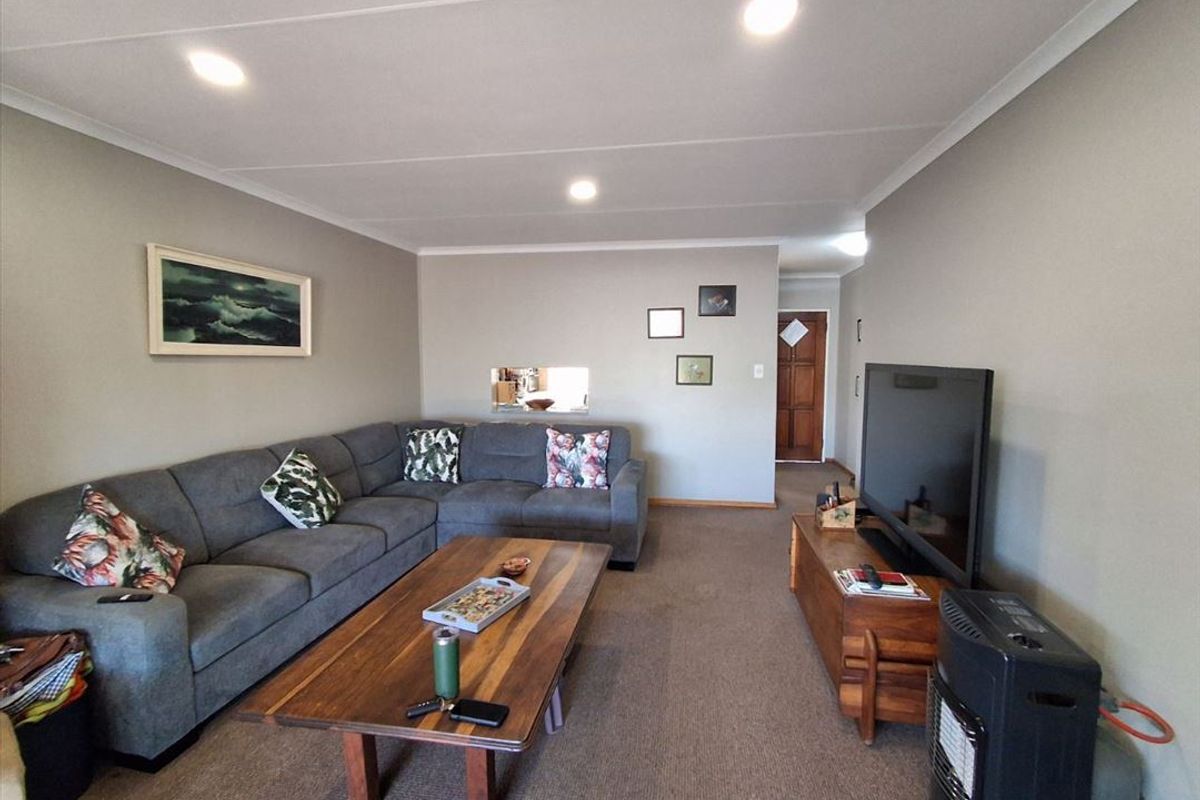 A comfortable living room featuring neutral walls, recessed downlighting, carpeted flooring, and a convenient pass-through window connecting to the adjacent kitchen area.