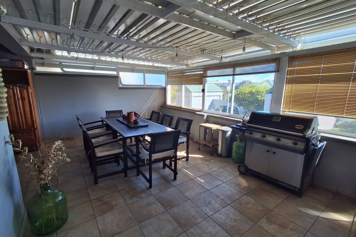 A covered outdoor patio area featuring tiled flooring, a corrugated metal roof, and large windows, providing a functional space for outdoor dining and entertaining.