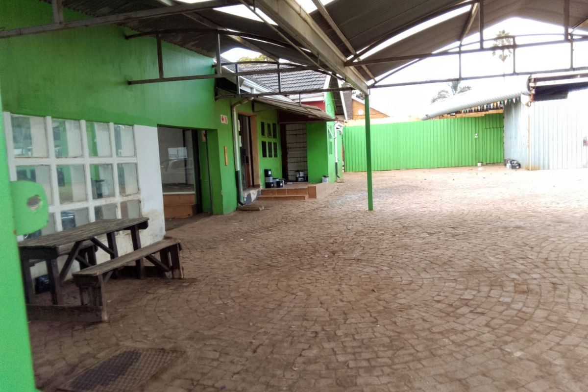 Spacious outdoor courtyard area featuring paved flooring, covered roofing structure, and green exterior walls, suitable for commercial use or outdoor storage.