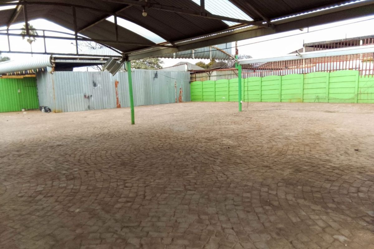 Large open-air utility or storage space featuring paved flooring, steel structural supports, and perimeter metal fencing under a corrugated roof structure.