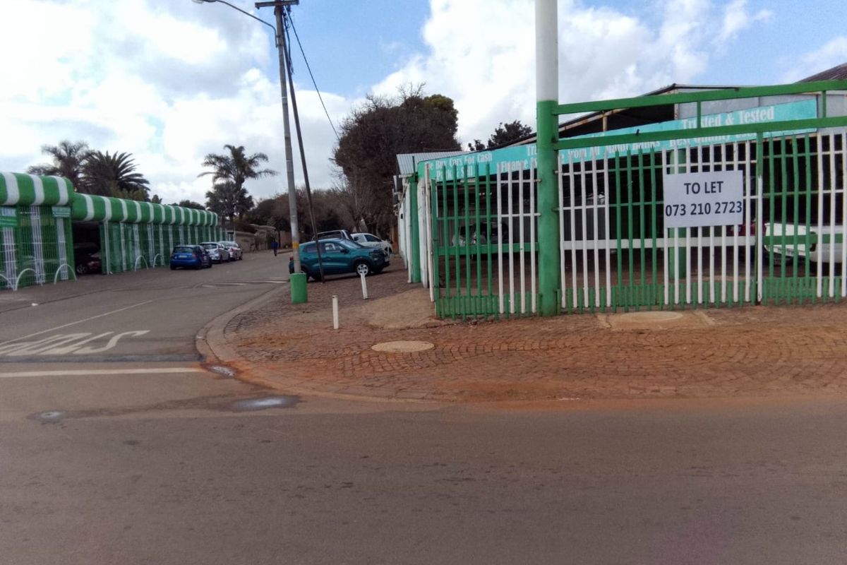 Street view of a commercial property featuring security fencing, gated access, and paved frontage, currently available for lease.