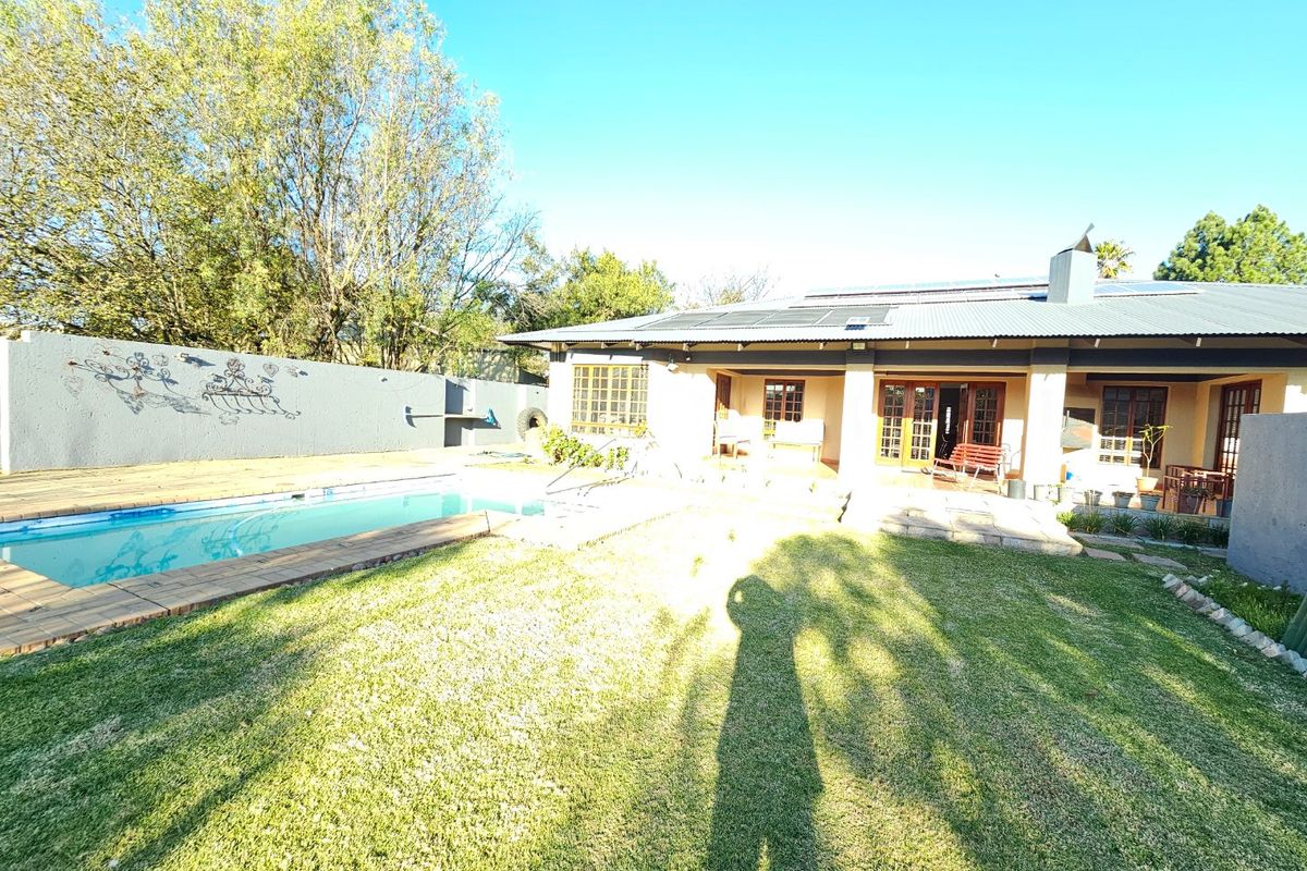 Rear view of the property featuring a swimming pool, a covered patio area, and a well-maintained garden with solar panels installed on the roof.