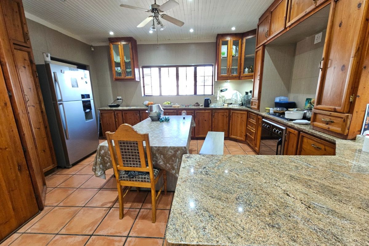 Spacious kitchen featuring extensive wooden cabinetry, granite countertops, built-in cooking appliances, and tiled flooring, offering a functional layout with ample storage space.