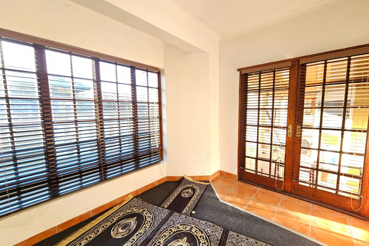A sunlit living area featuring terracotta floor tiles, wooden window and door frames, and fitted venetian blinds, offering a blank canvas for interior design.