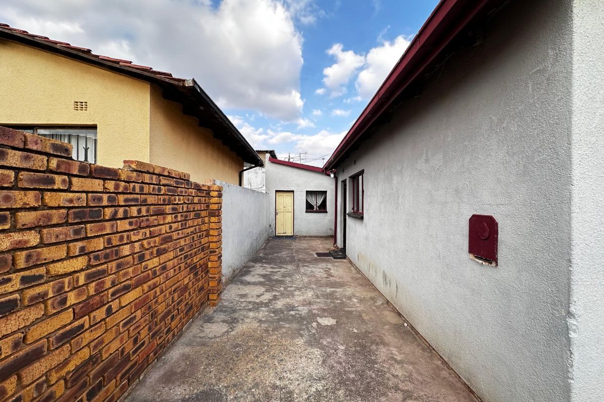 A narrow exterior side passage featuring concrete paving, enclosed by a brick boundary wall and the side elevation of the main dwelling.