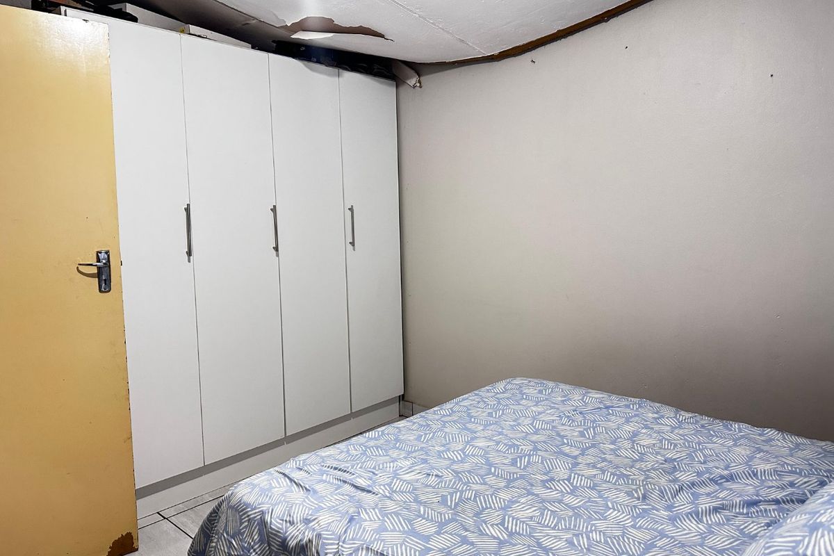 A bedroom featuring a built-in wardrobe and tiled flooring, currently showing signs of ceiling damage and wear on the door finish.