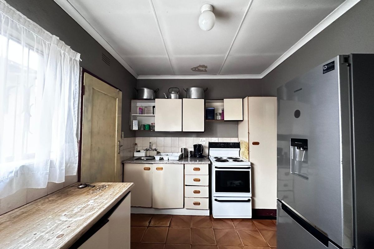 A functional kitchen featuring built-in cabinetry, laminate countertops, a stainless steel sink, and a freestanding stove with tiled flooring and backsplash.