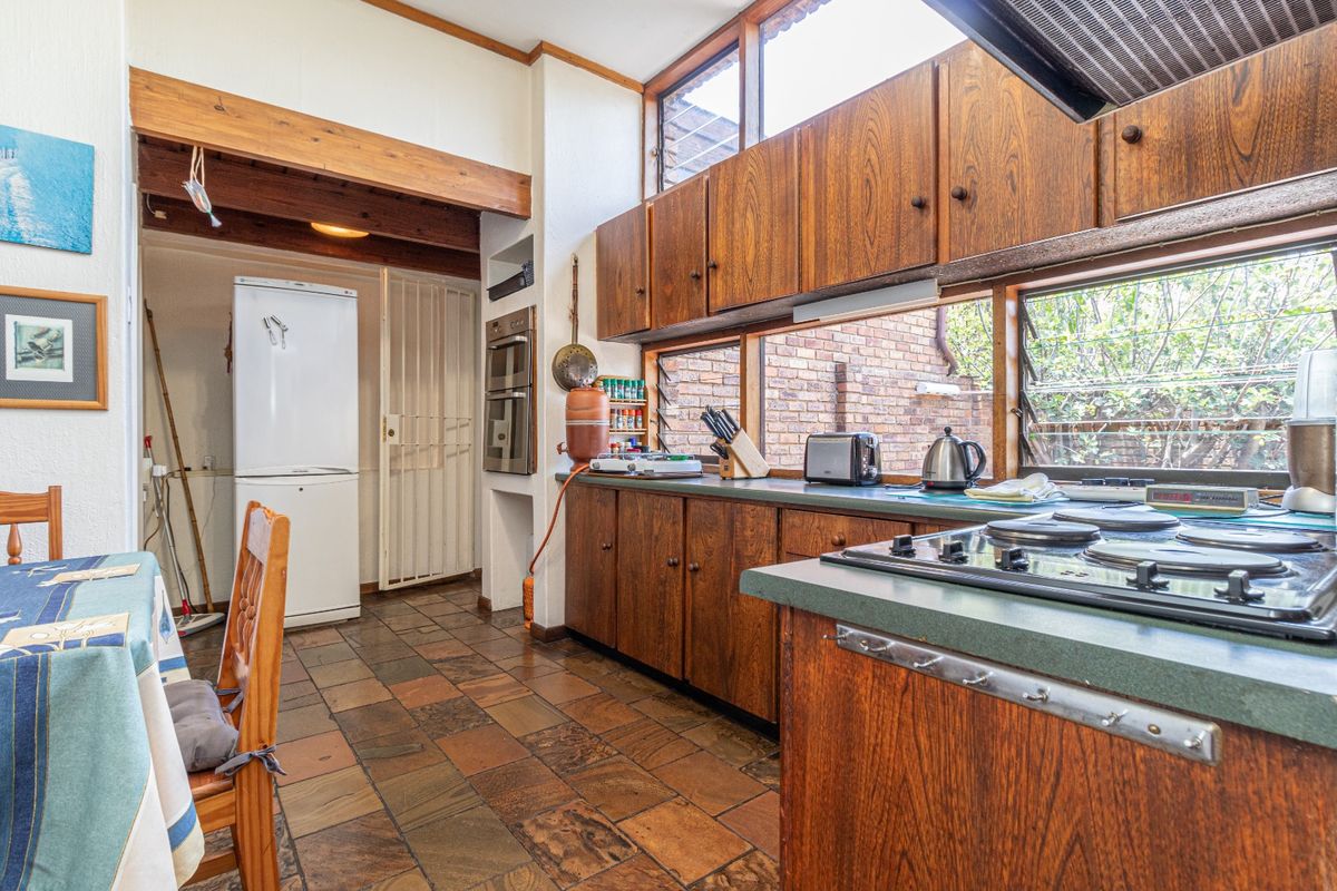 A functional kitchen featuring original wooden cabinetry, stone tile flooring, exposed timber beams, and built-in appliances, offering potential for a modern renovation.