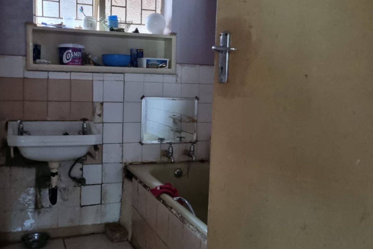 A dated bathroom featuring a wall-mounted basin and built-in bathtub, requiring significant renovation and repair to the tiled surfaces and fixtures.
