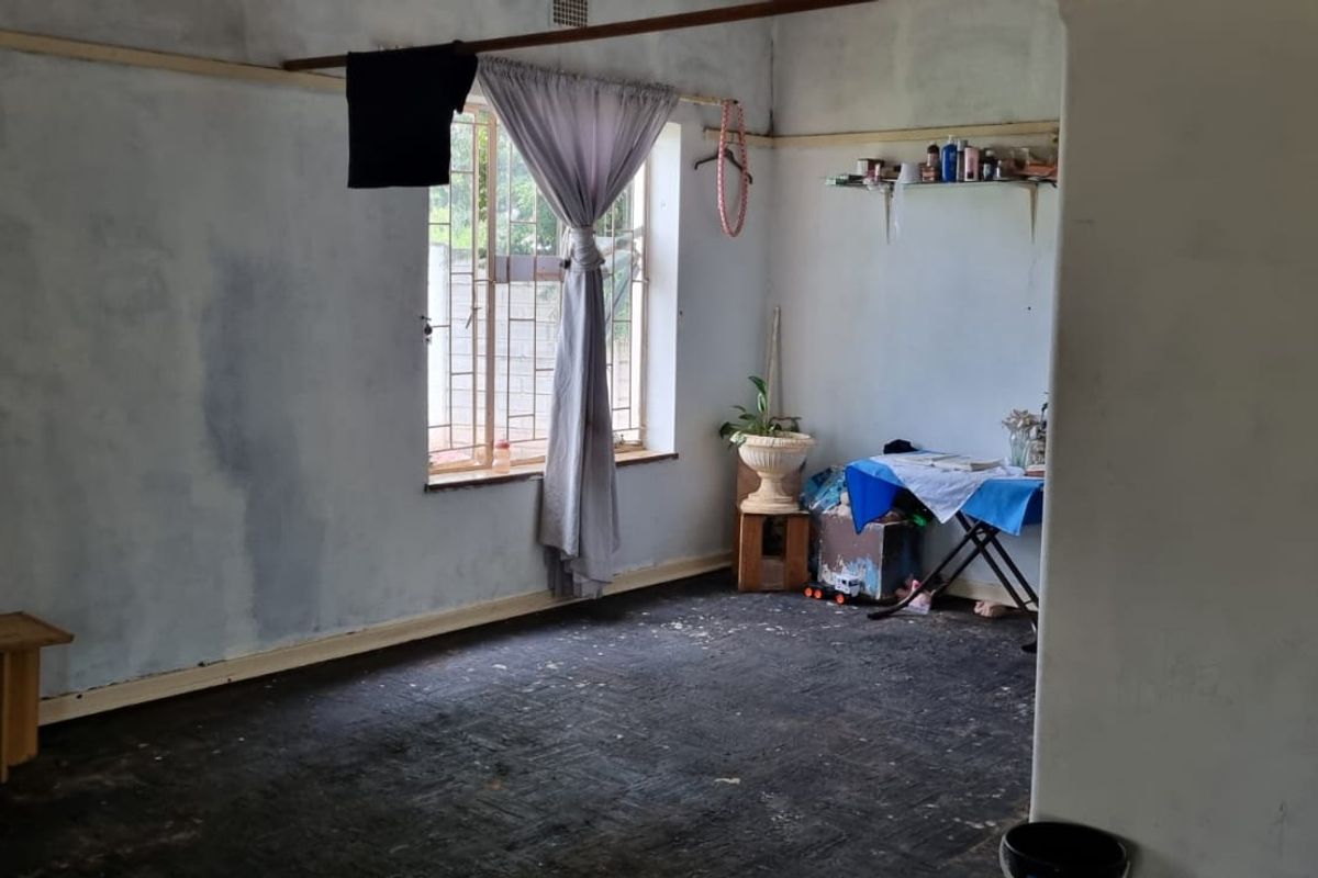A vacant bedroom featuring security bars on the window, requiring significant cosmetic updates including flooring replacement and wall refinishing.