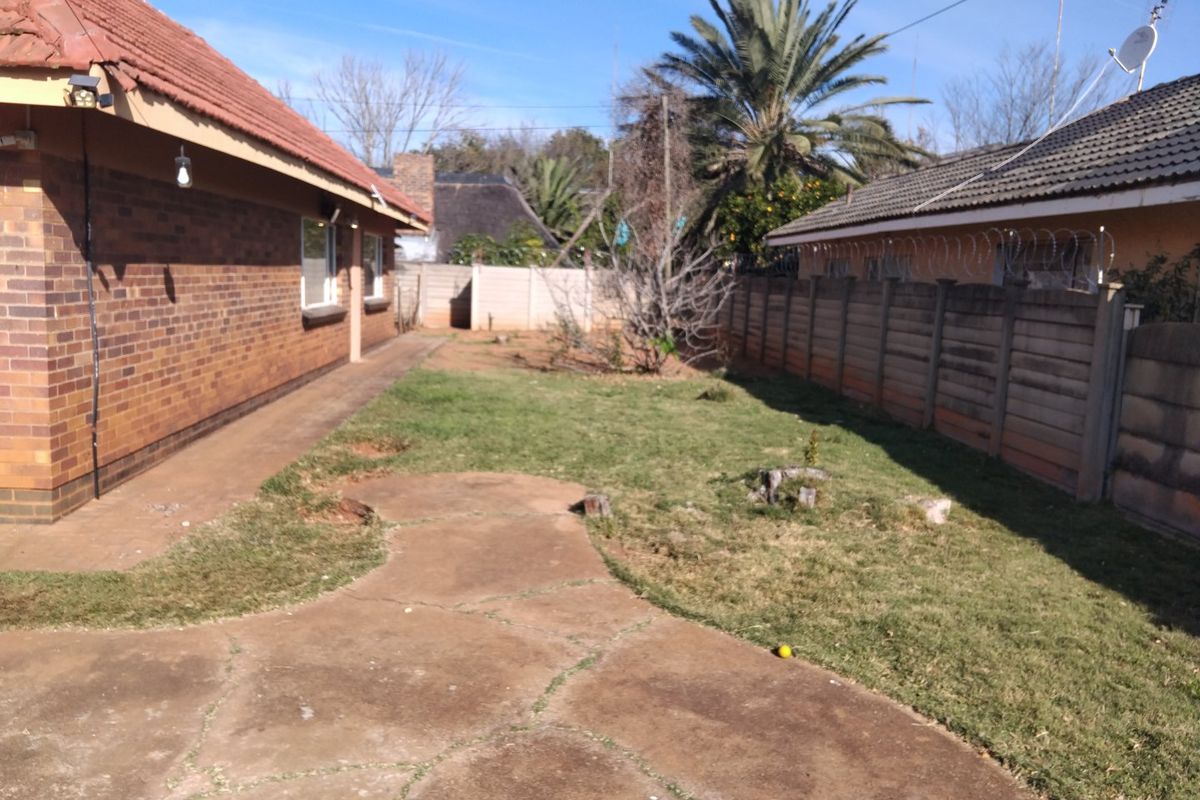 A rear exterior view of the property featuring a brick facade, tiled roof, paved patio area, and a fenced garden with a precast boundary wall.