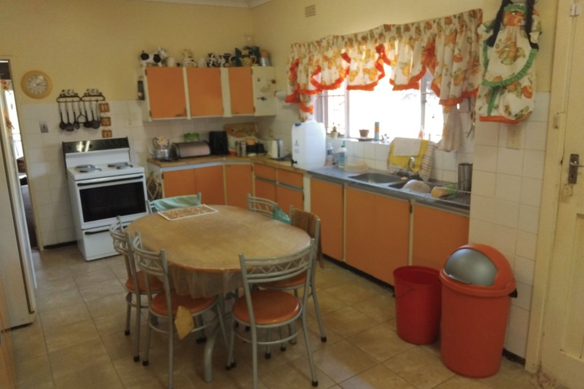 A dated kitchen featuring original orange cabinetry, tiled flooring, and a freestanding stove, offering significant potential for a modern renovation.