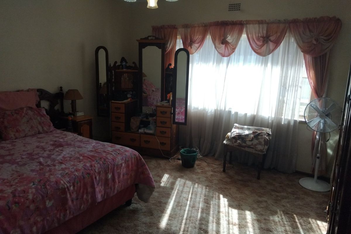 A bedroom featuring carpeted flooring and a large window with natural light, requiring cosmetic updates to modernize the space.