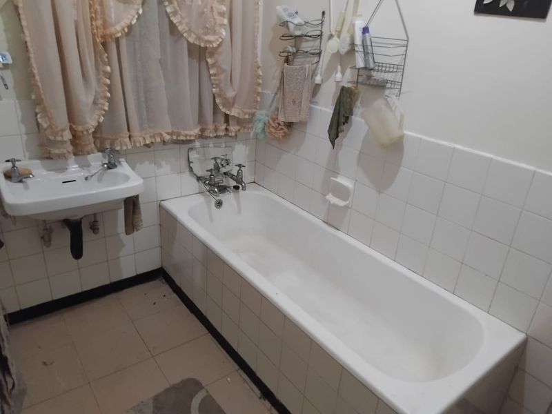 A functional bathroom featuring a standard bathtub, wall-mounted basin, and tiled surfaces, currently presenting in a dated condition suitable for renovation.