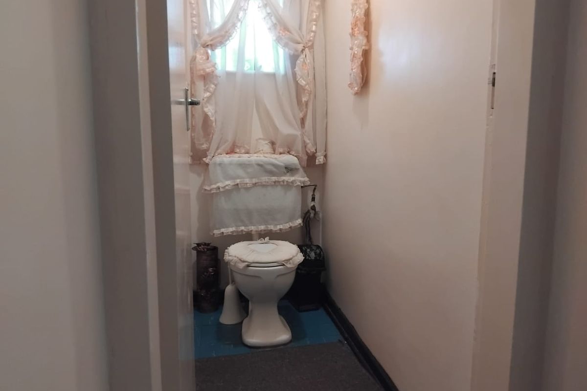 A compact bathroom featuring a standard toilet and cistern, finished with painted flooring and a window for natural light.