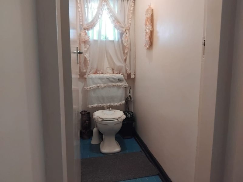 A compact bathroom featuring a standard toilet and cistern, finished with painted flooring and a window for natural light.