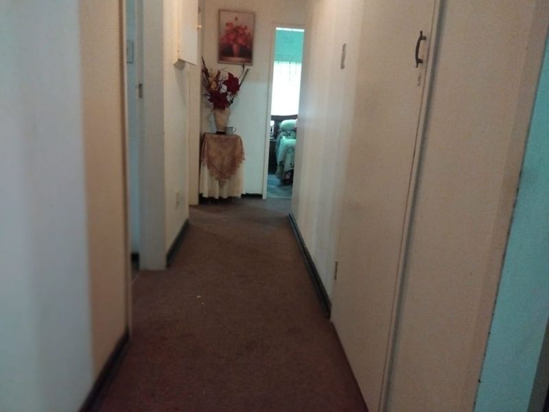 A narrow residential hallway featuring built-in storage cupboards and carpeted flooring, providing access to adjacent rooms.
