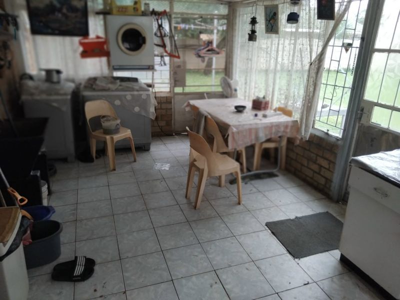 A functional laundry and utility area featuring tiled flooring, brick walling, and large windows providing natural light and garden access.