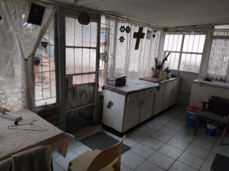 A dated scullery or utility area featuring built-in cabinetry, tiled flooring, and large windows with security bars, offering potential for renovation.