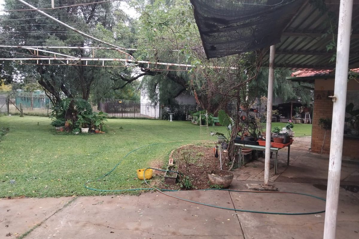 Spacious rear garden featuring a covered concrete patio area, established trees, and secure perimeter fencing, offering potential for outdoor entertainment development.