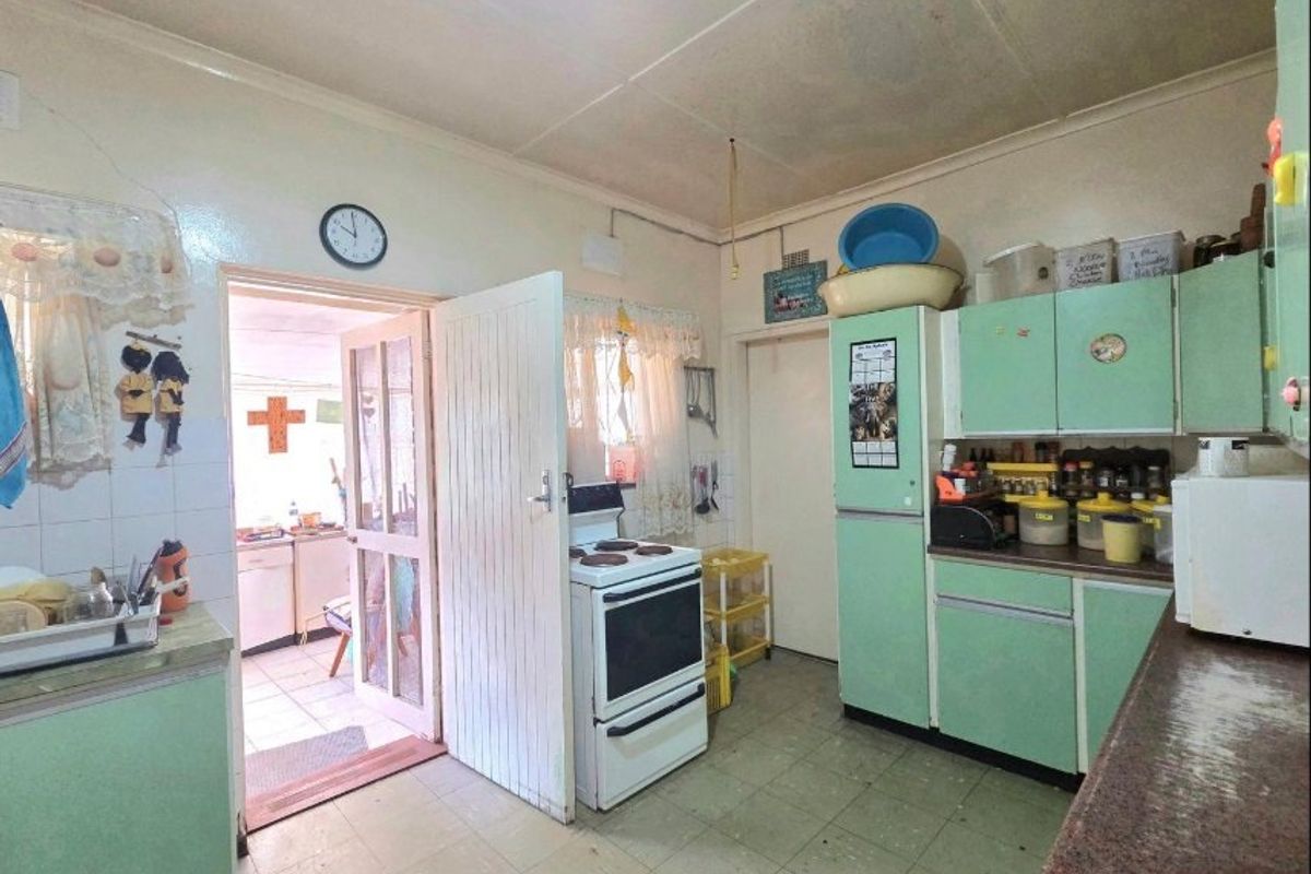A dated kitchen featuring original cabinetry, a freestanding stove, and tiled flooring, offering significant potential for modernization and renovation.