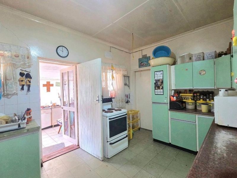 A dated kitchen featuring original cabinetry, a freestanding stove, and tiled flooring, offering significant potential for modernization and renovation.