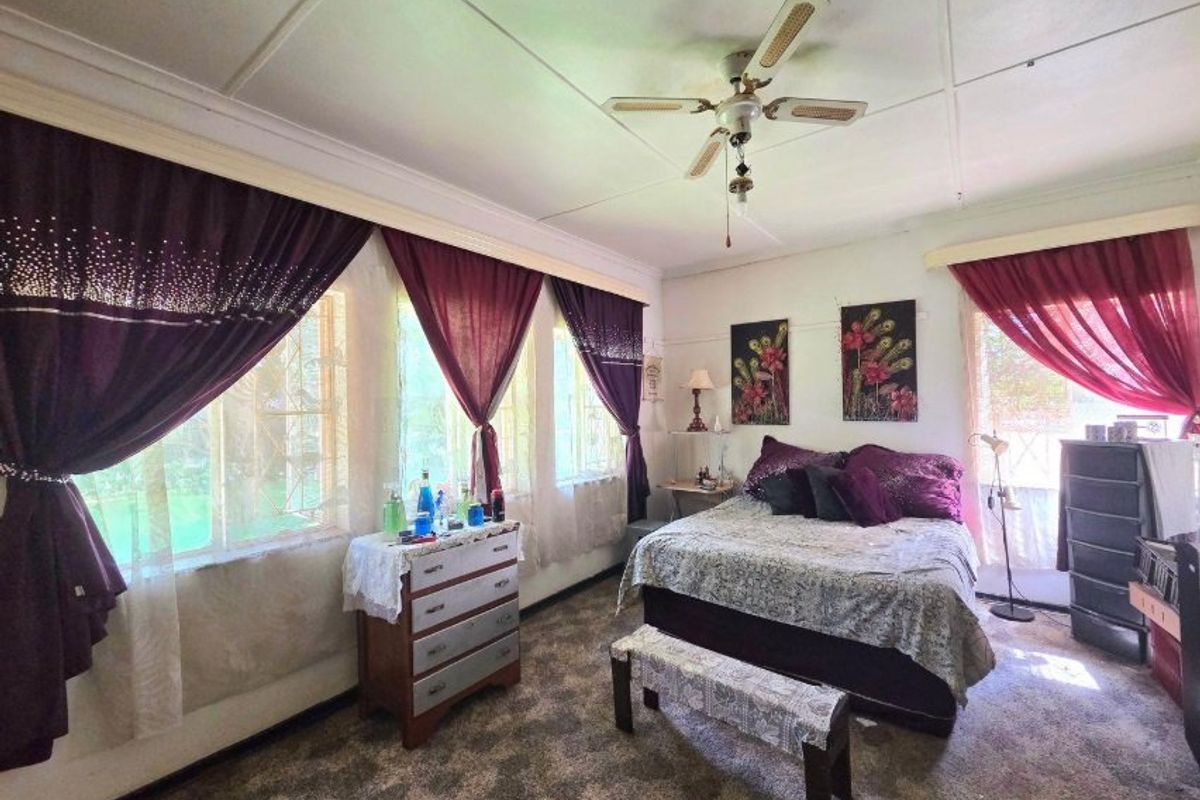 A bedroom featuring a ceiling fan and large windows with security bars, currently finished with dated carpet and ceiling treatments.