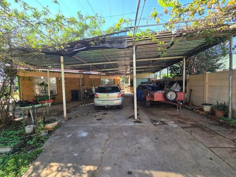 A large outdoor carport area with a metal roof structure, concrete flooring, and perimeter boundary walling, providing covered parking space.