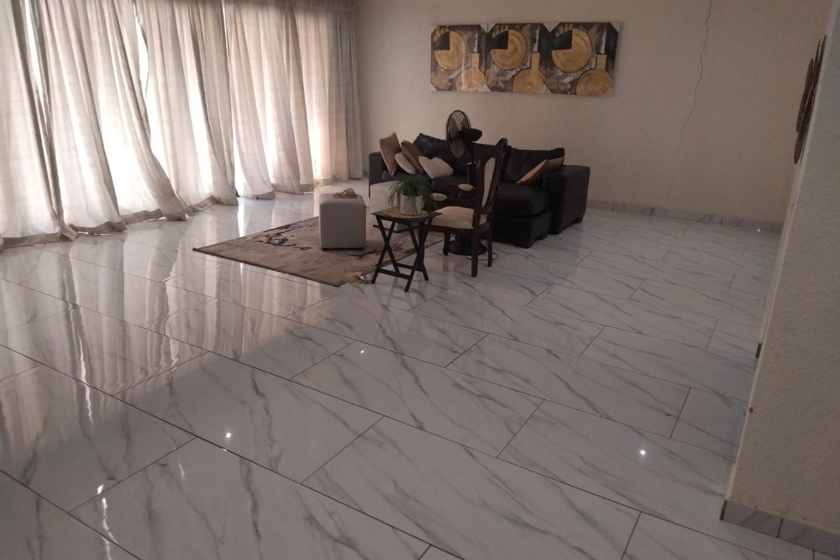 Spacious living area featuring polished marble-look floor tiles, recessed lighting, and large windows with full-length curtains.