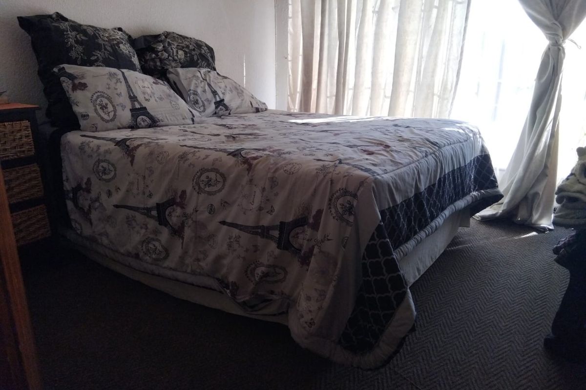 A bedroom featuring carpeted flooring and natural light provided by large windows with curtains.