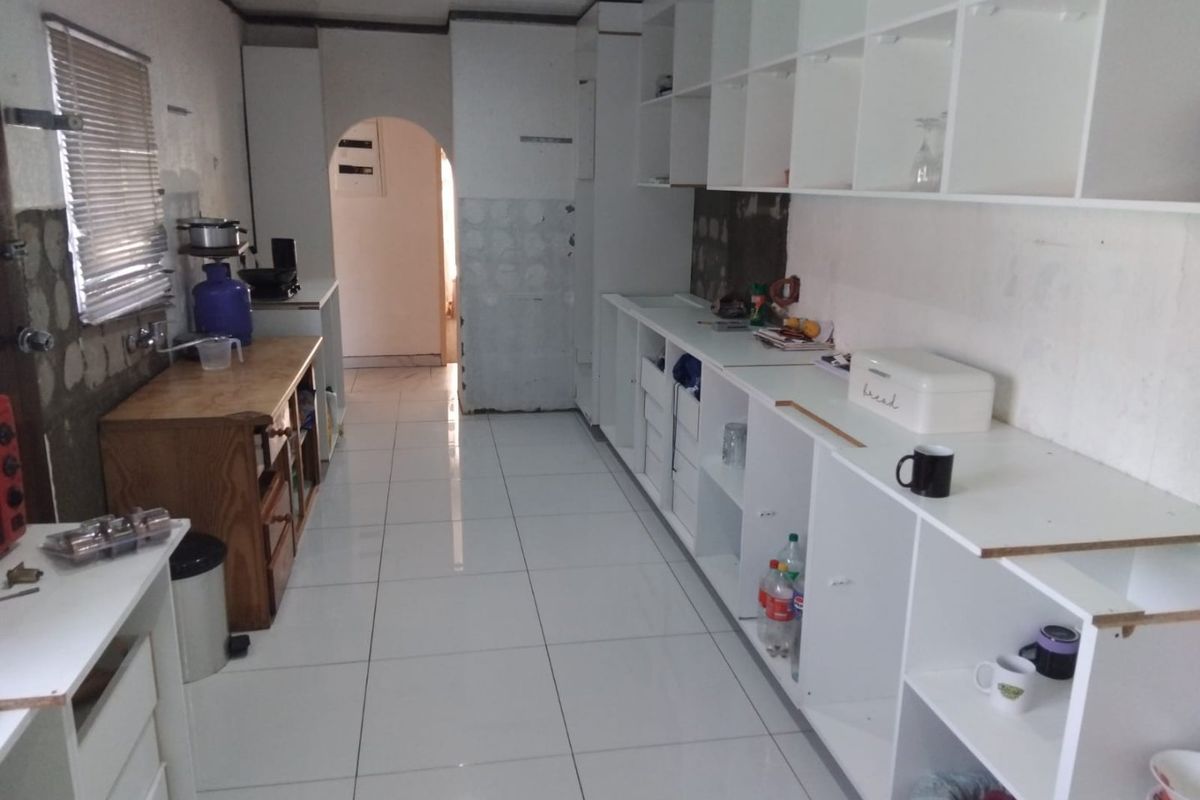 A kitchen space featuring white tiled flooring and extensive open shelving, currently in an unfinished state requiring cabinetry completion and wall finishing.