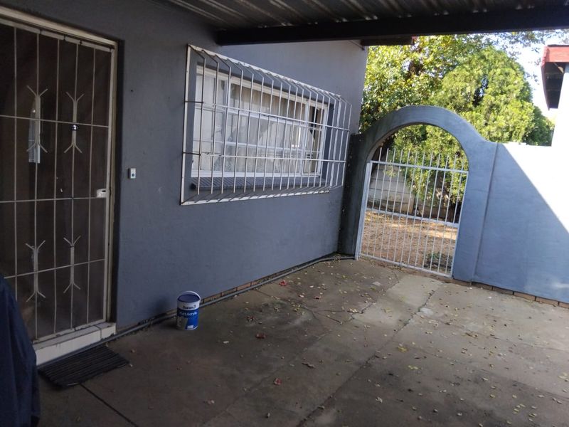 Covered patio area featuring concrete flooring, security gates, and an arched garden entrance, providing a functional outdoor space for the townhouse.