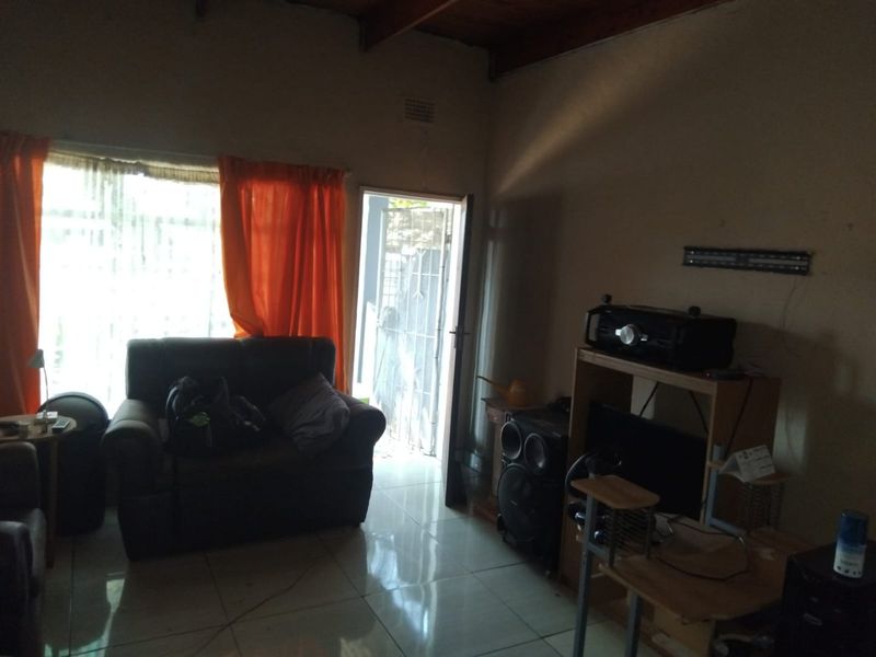 A living room featuring tiled flooring and exposed timber ceiling beams, with direct access to an exterior area through a security gate.