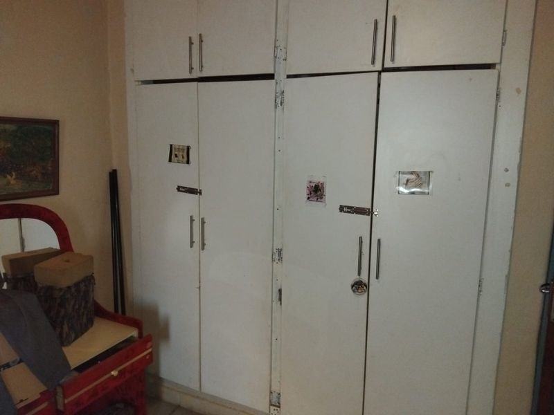 A bedroom featuring floor-to-ceiling built-in cupboards with white doors, showing signs of wear and tear on the cabinetry.