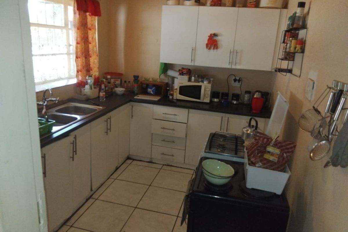 A functional kitchen featuring white cabinetry, dark laminate countertops, a double basin sink, and tiled flooring, offering potential for modernization.