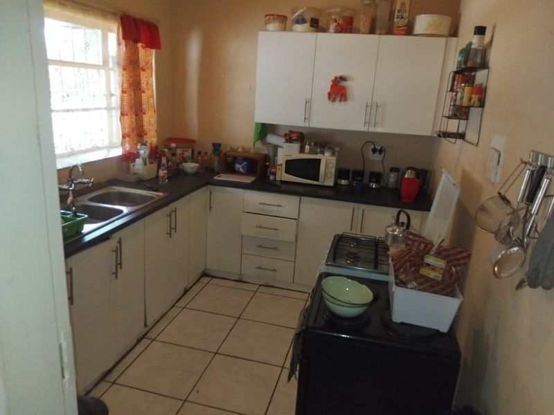 A functional kitchen featuring white cabinetry, dark laminate countertops, a double basin sink, and tiled flooring, offering potential for modernization.