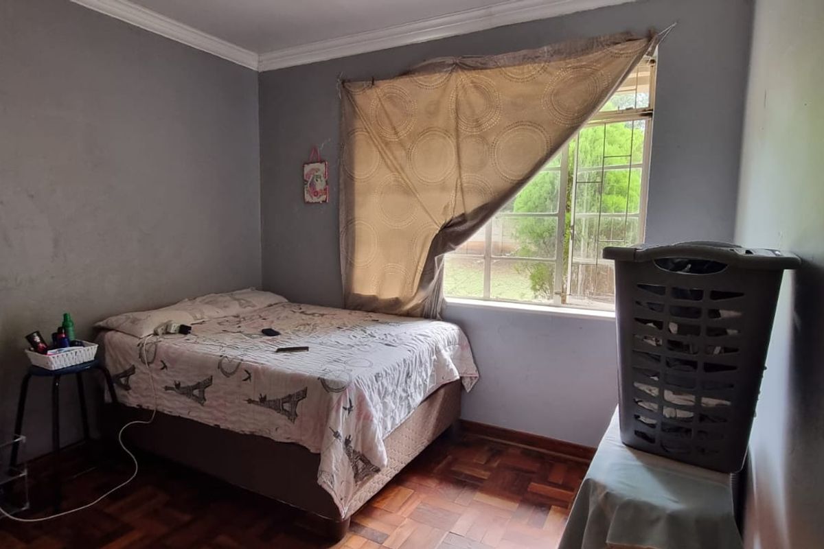 A bedroom featuring parquet flooring, a window with security bars, and coving, requiring cosmetic updates to the wall finishes.