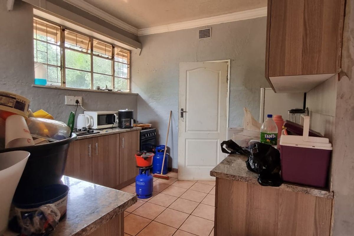 A functional kitchen featuring laminate cabinetry, tiled flooring, and a steel window frame, currently requiring cosmetic updates to the wall finishes.