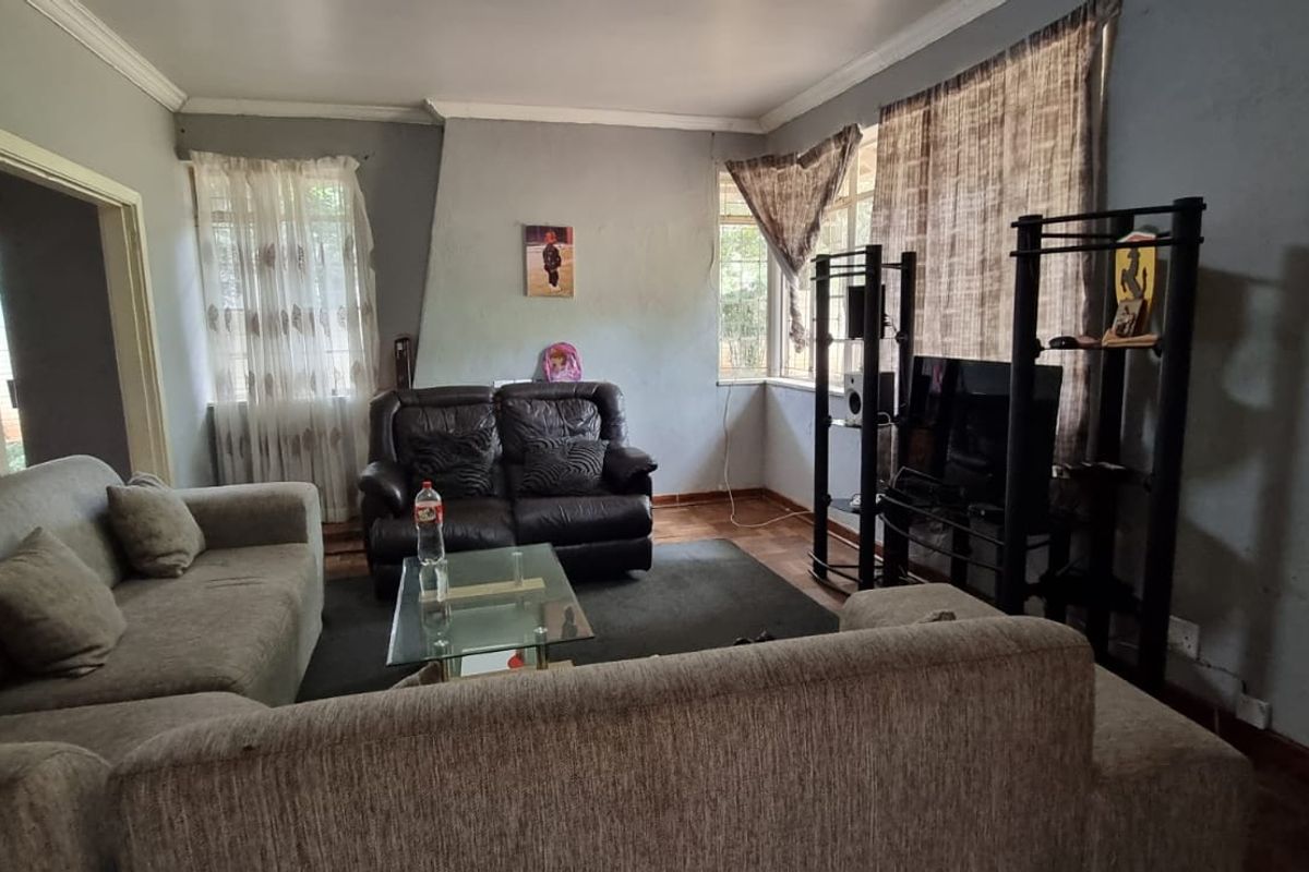 A living room featuring crown molding and wooden flooring, currently showing signs of wear on the walls.