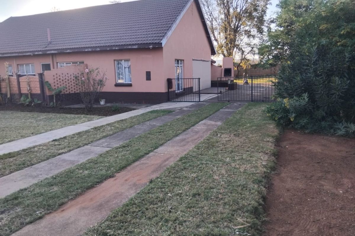 Rear exterior view of the house featuring a concrete driveway, brick boundary wall, security gates, and a built-in outdoor braai area.