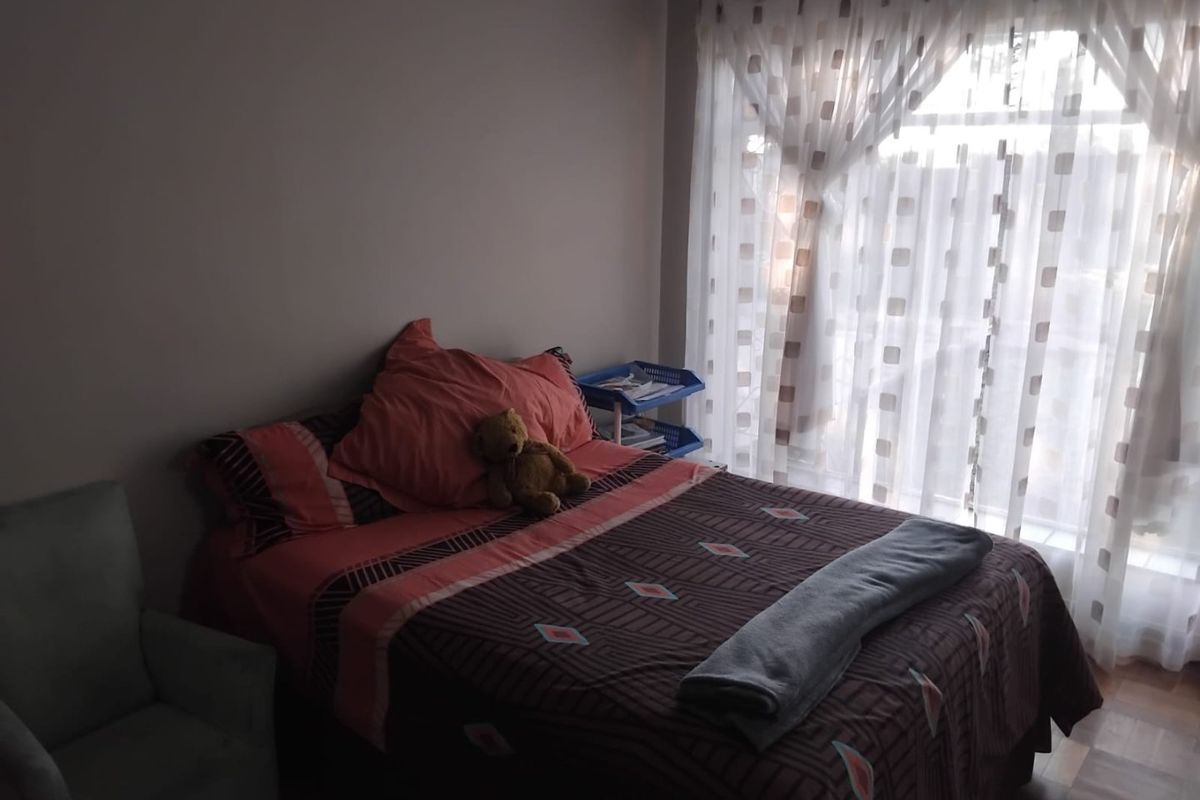 A bedroom featuring parquet flooring and a large window with sheer curtains, providing natural light to the space.