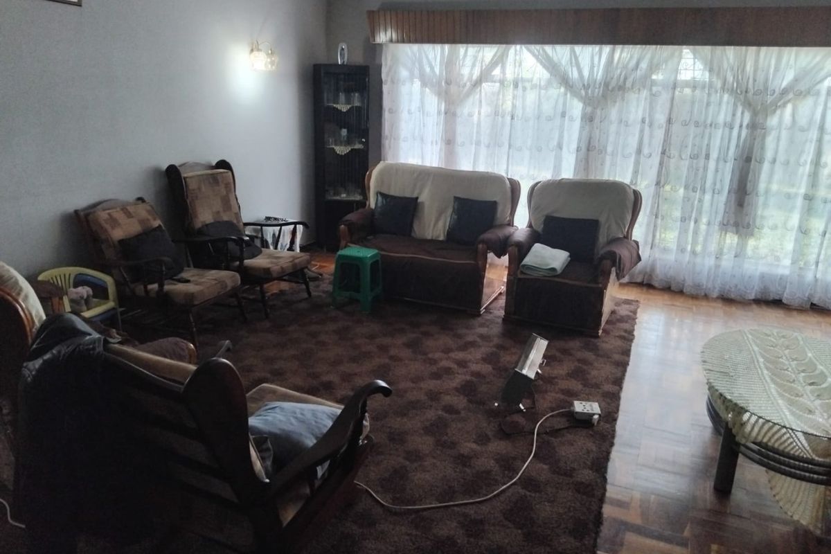 A spacious living room featuring classic parquet flooring and a large window with sheer curtains, offering a traditional layout with potential for modernization.