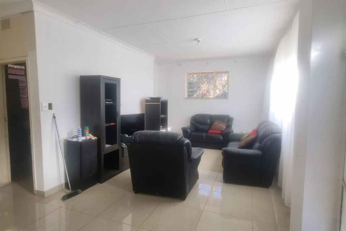A living room featuring tiled flooring and neutral walls, providing a functional space with natural light and security features on the window.