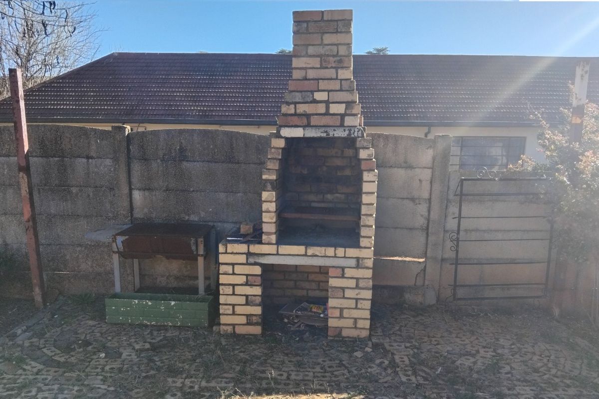 Outdoor rear area featuring a built-in brick braai, paved flooring, and a precast concrete boundary wall.