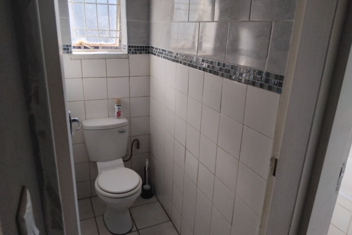 A compact, tiled bathroom featuring a standard toilet and a small window with security bars, requiring cosmetic updates to improve its dated appearance.