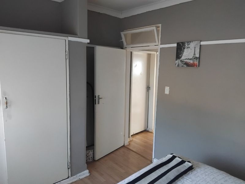 A bedroom featuring built-in cupboards, laminate flooring, and a transom window above the doorway, providing access to the hallway.